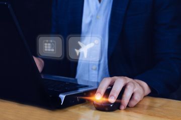 Person in a suit using a laptop and a mouse, with digital icons floating above the keyboard.